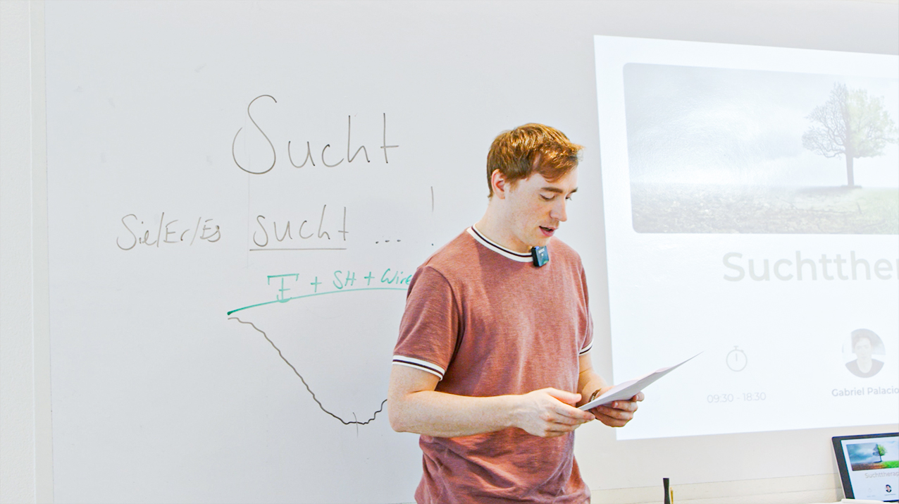 Gabriel Palacios präsentiert stehend vor einer Wand, neben einer Projektion des Beamers.